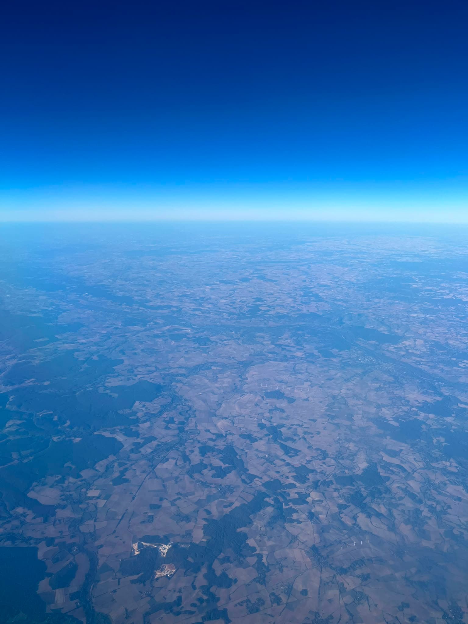A clear blue sky meeting the horizon above a patchwork of countryside